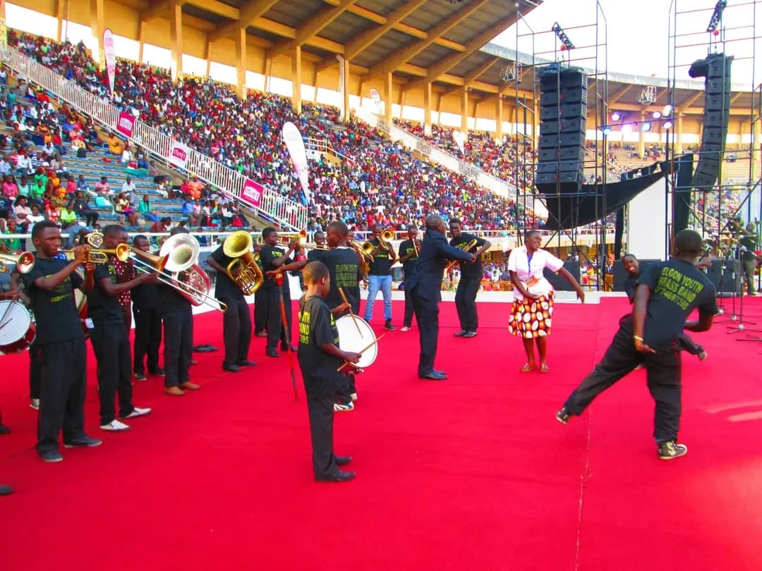 Elgon Youth Brass Band performing on a red stage at a packed stadium